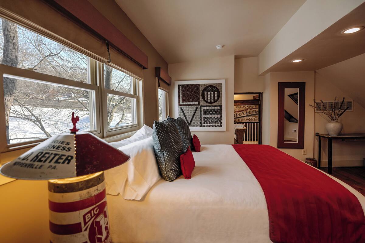 A hotel room with a large bed, a window with a rooster decoration, and a wall with abstract art.