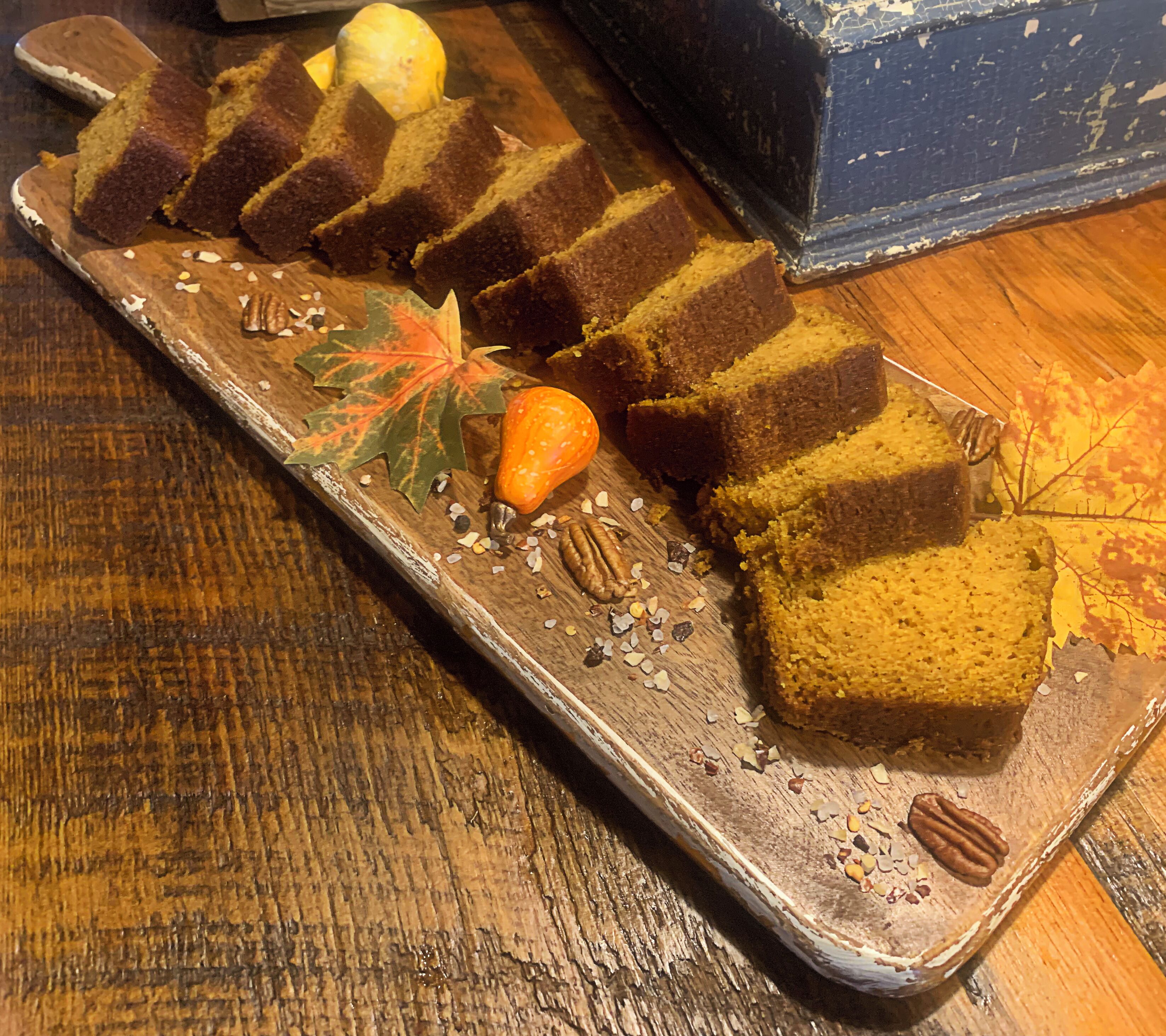 A tray with slices of pumpkin cake, a pumpkin, and some nuts on a wooden surface.