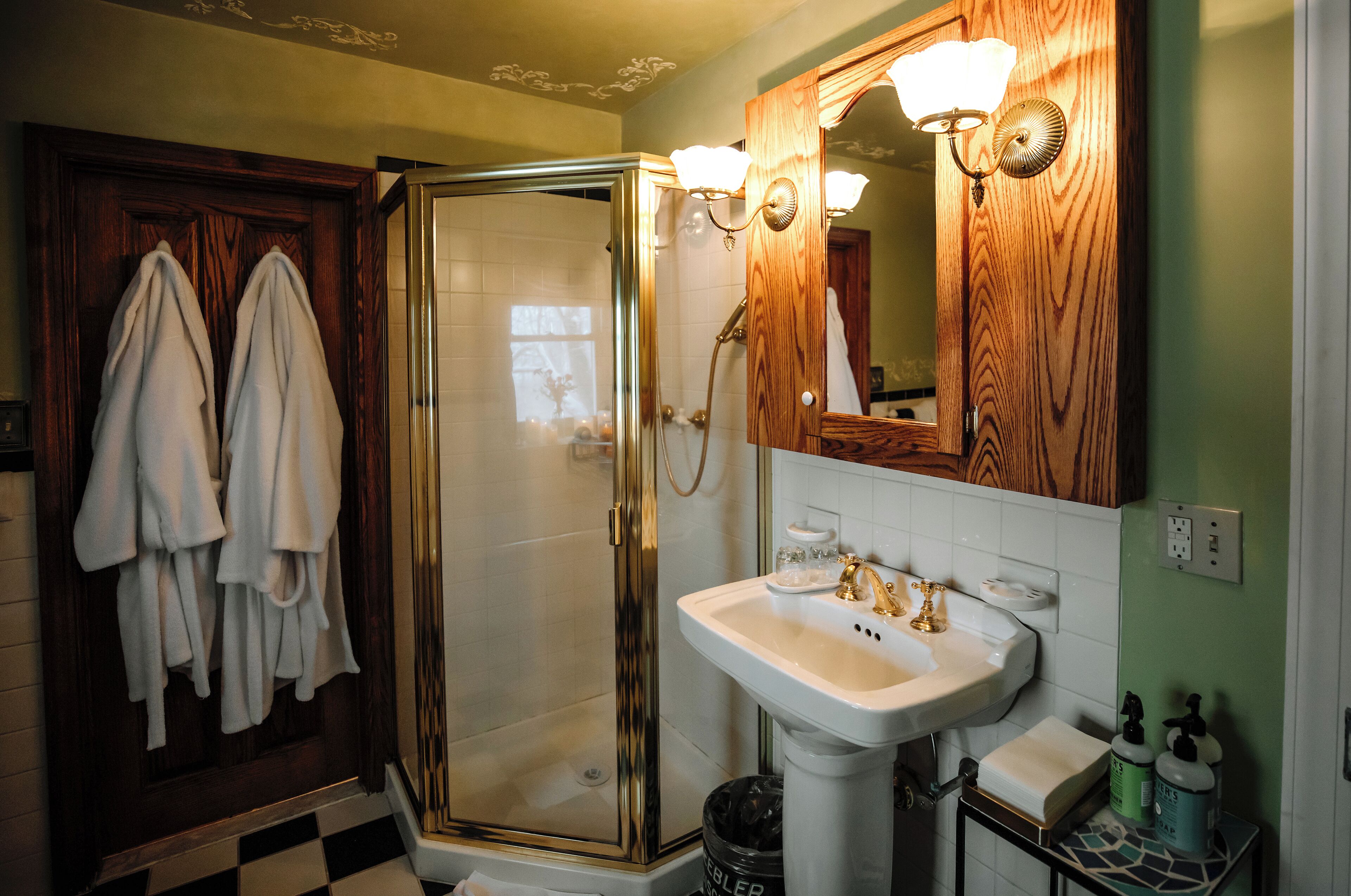A bathroom with a glass-enclosed shower, a sink with a mirror above it, and towels hanging on a door.