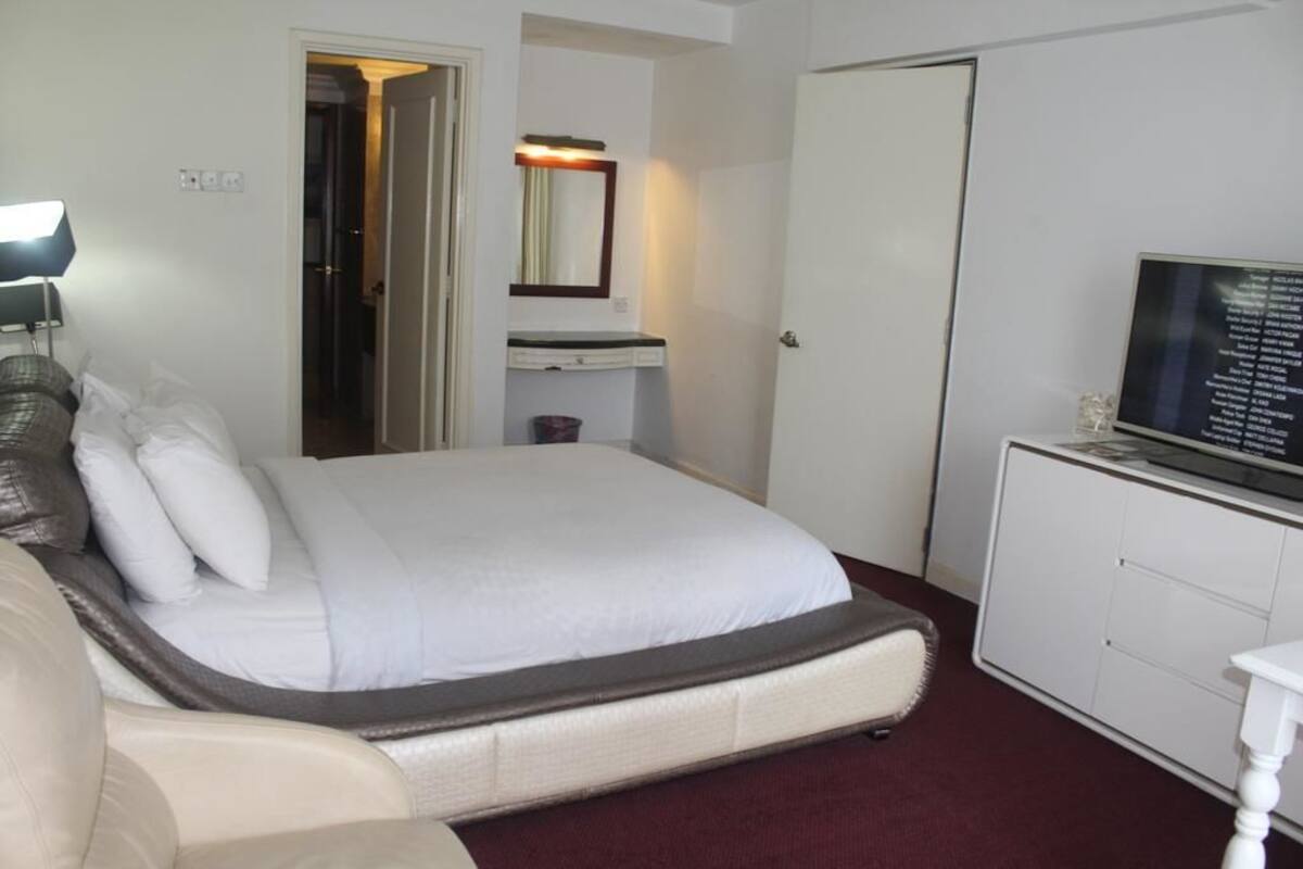 A hotel room with a bed, a television on a cabinet, a mirror above the sink, and a door leading to another room.