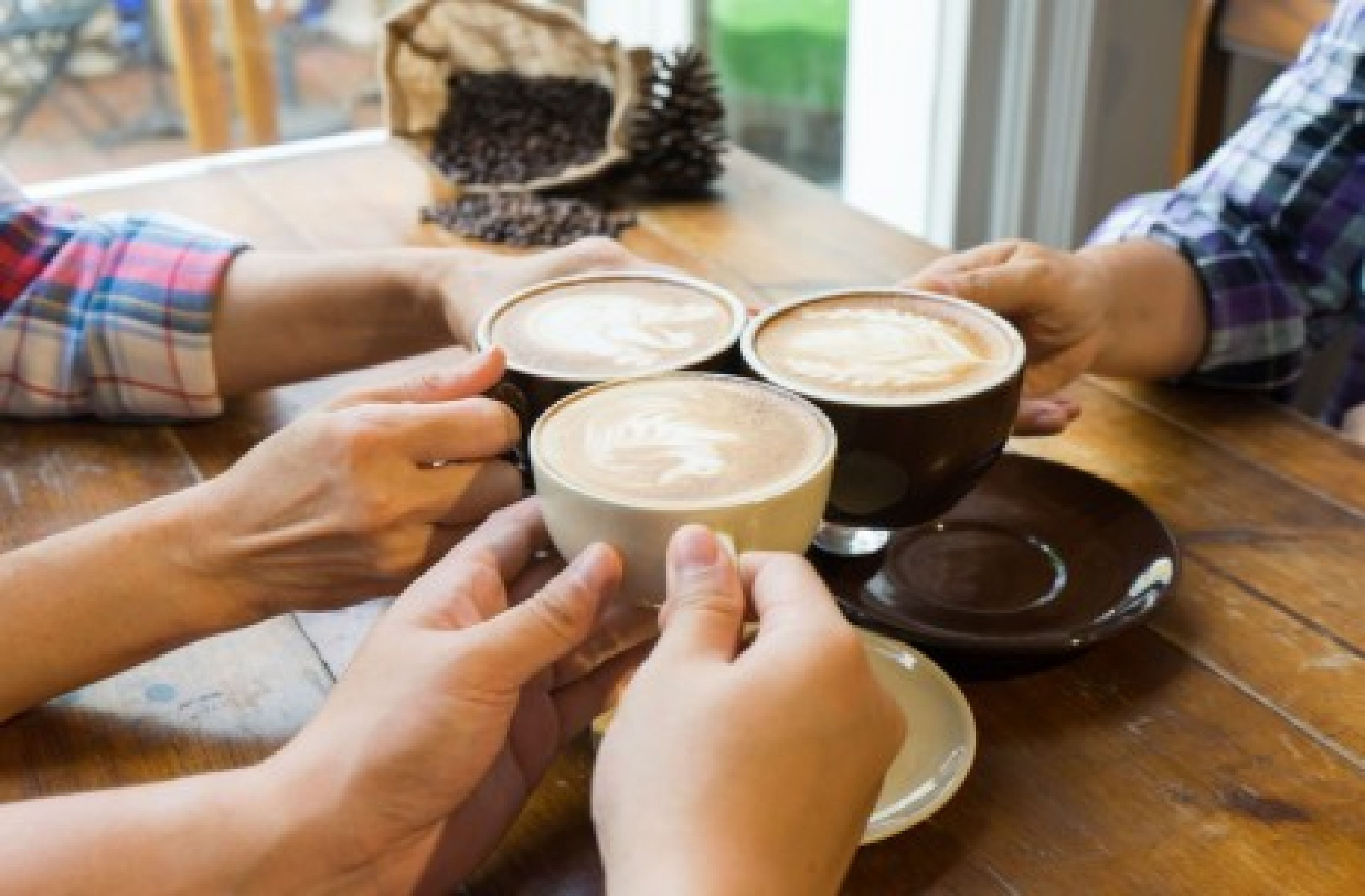 A group of people holding coffee cups at a wooden table.