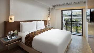 Habitación de hotel con una cama grande, un escritorio con lámpara y vistas a un balcón con barandilla.
