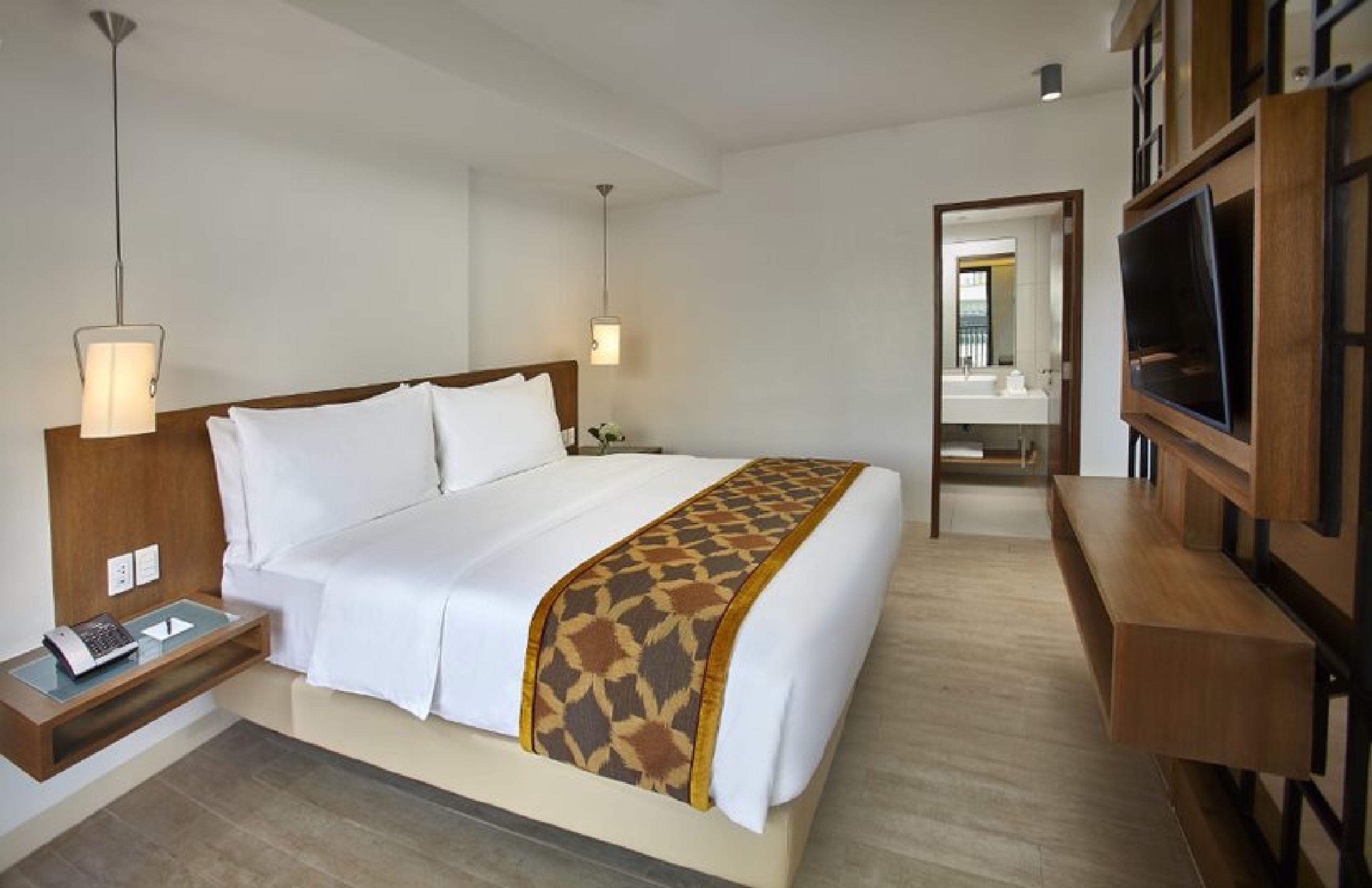 A hotel room with a bed, bedside table, lamp, TV, and a mirror.