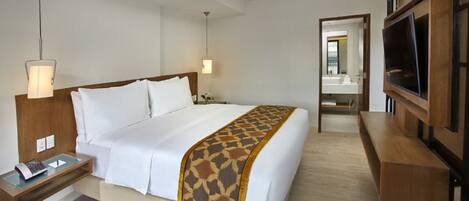 A hotel room with a bed, bedside table, lamp, TV, and a mirror.