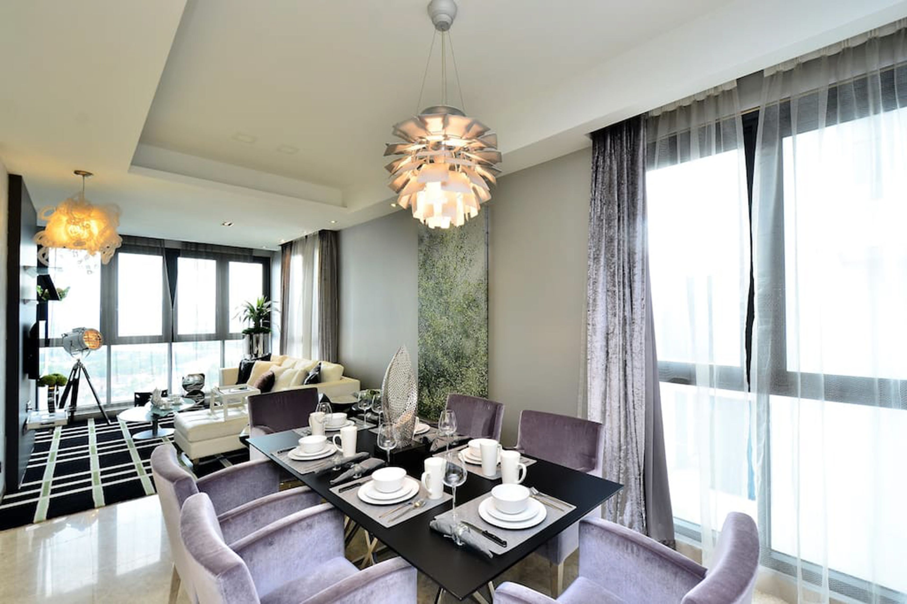 A modern dining area with a black table set for four, surrounded by purple chairs. There are two pendant lights above the table, and a large window with sheer curtains is visible to the right.