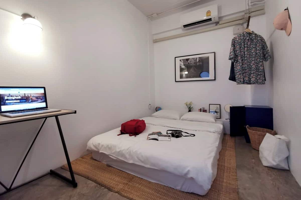A bedroom with a bed, a laptop on a desk, a red bag, and a hanging shirt.