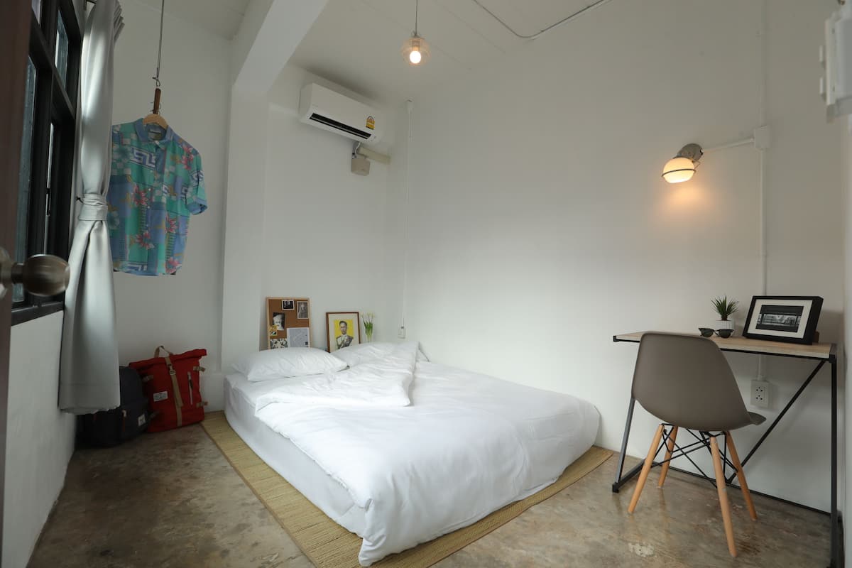 A bedroom with a bed, a desk, a chair, an air conditioner, and a hanging garment.