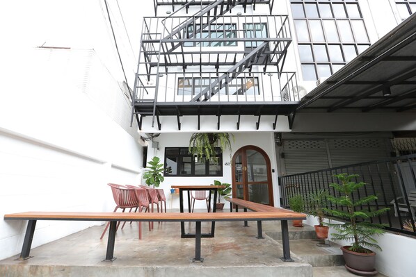 A courtyard with a wooden bench, chairs, and potted plants.
