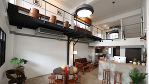 A spacious loft-style living area with a high ceiling, a mezzanine level, and a kitchen area.