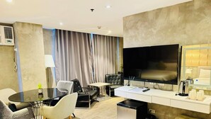 Een moderne hotelkamer met een flatscreen televisie, een bureau met koffiezetapparaat, een minibar en een comfortabele zithoek met een bank en stoelen.