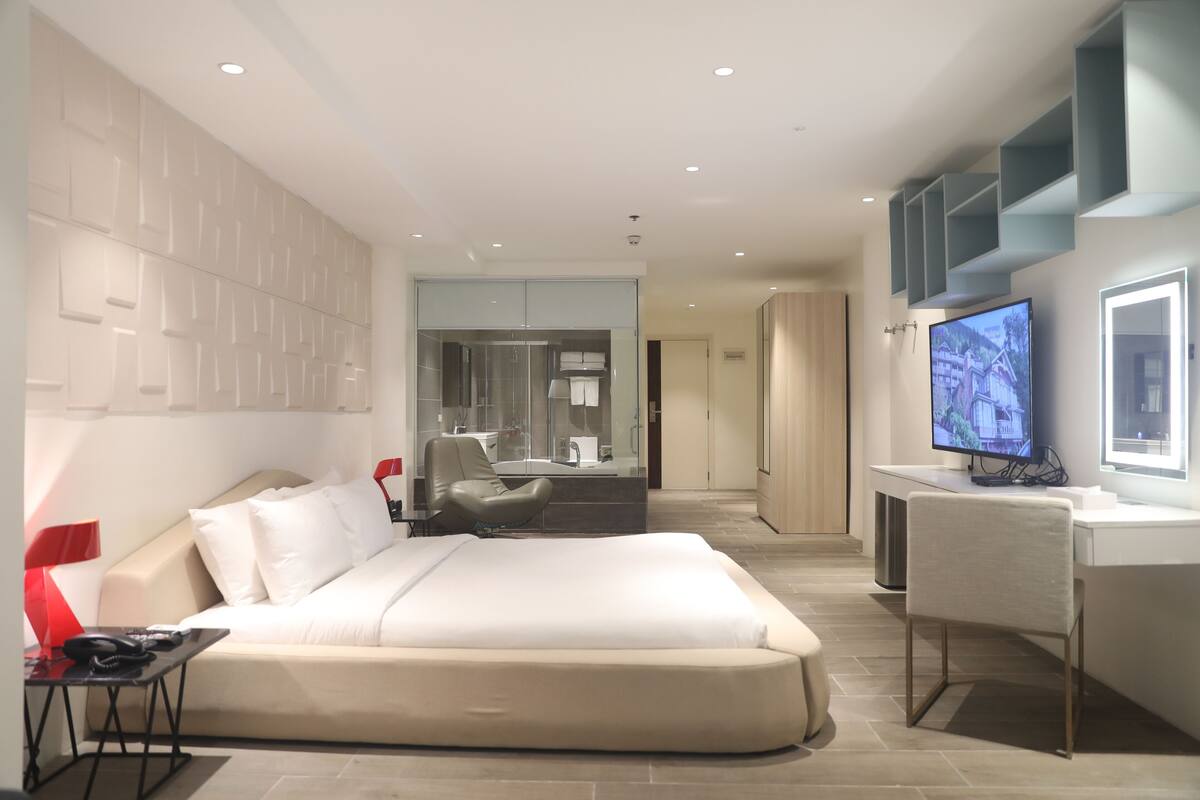 Een moderne hotelkamer met een groot bed, een bureau met een computer, een televisie en een badkamer met een glazen scheidingswand.