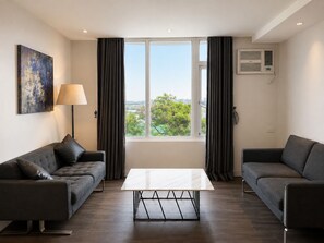 Een moderne woonkamer met twee banken, een salontafel, een lamp en een groot raam met gordijnen.