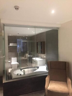 Een moderne badkamer met een douchecabine van glas, een grote spiegel en een bruine stoel.