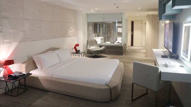 Een moderne hotelkamer met een groot bed, een bureau met een computer, een stoel, een televisie en een badkamer met een spiegel en wastafel.
