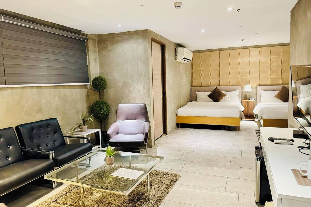 Een moderne hotelkamer met een bank, fauteuil, glazen salontafel en een bed met hoofdeinde.