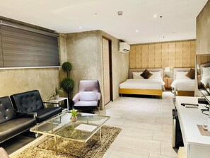 Een moderne hotelkamer met een bank, fauteuil, glazen salontafel en een bed met hoofdeinde.