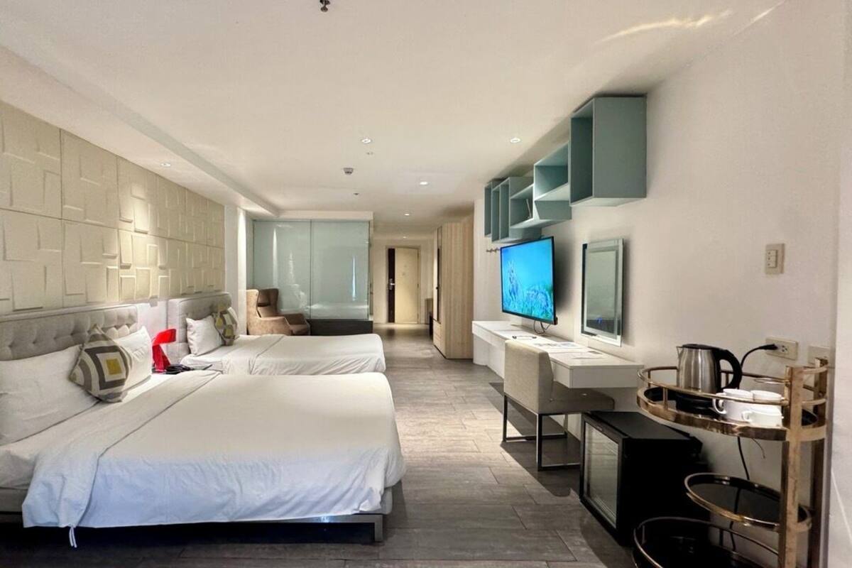 Een hotelkamer met twee bedden, een televisie, een bureau met een computer en een kitchenette.