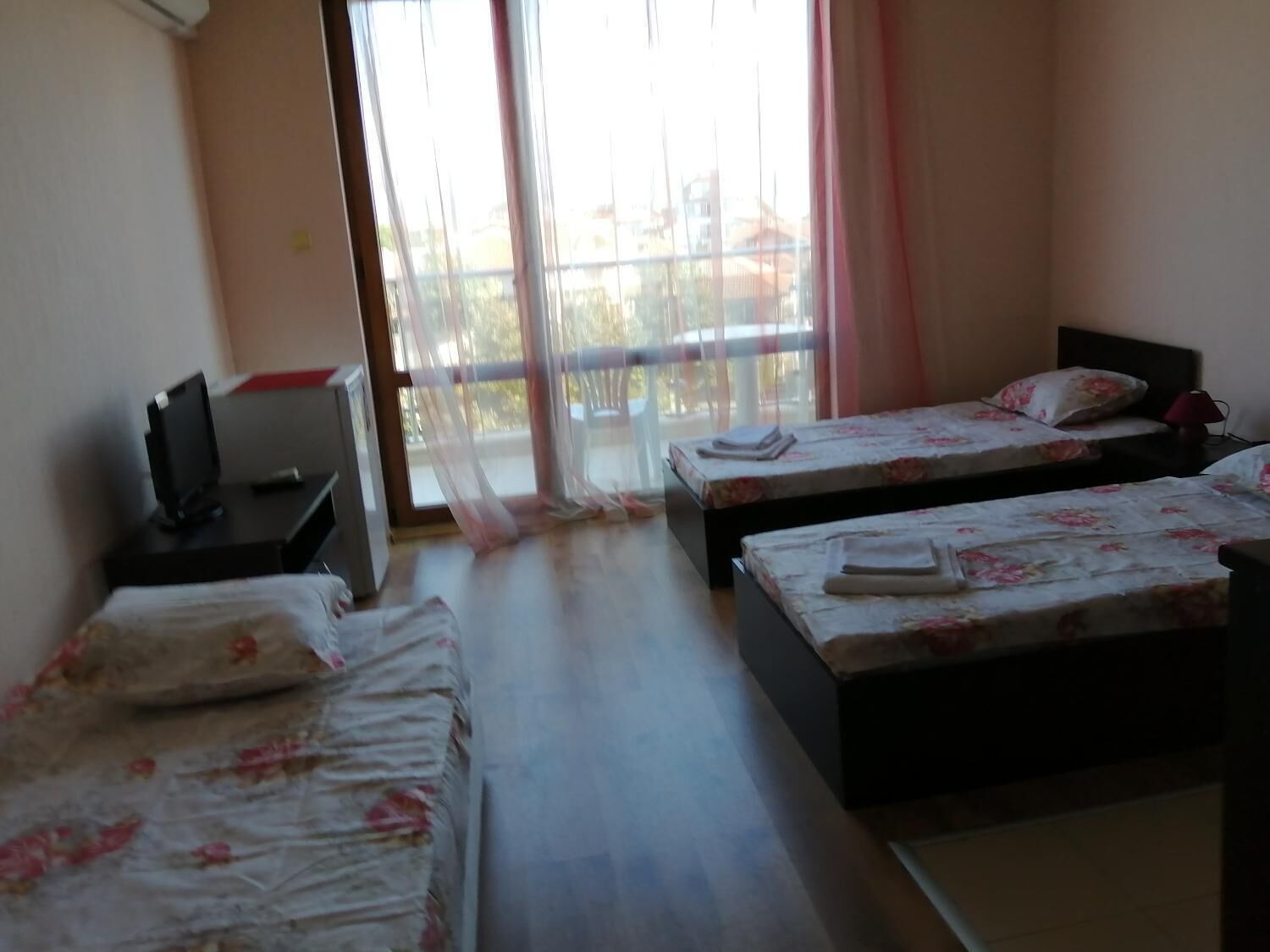 A hotel room with two single beds, a desk with a computer, and a large window with sheer curtains.