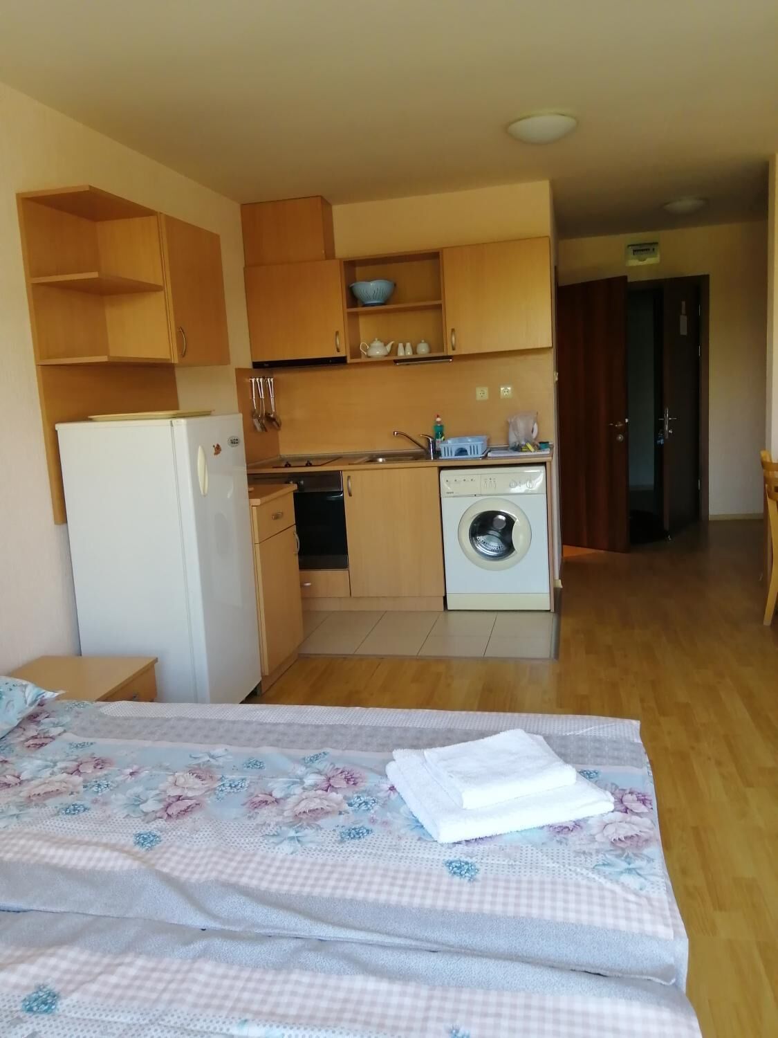 Ein kleines Zimmer mit Bett, einer kleinen Küchenzeile und einer Waschmaschine.