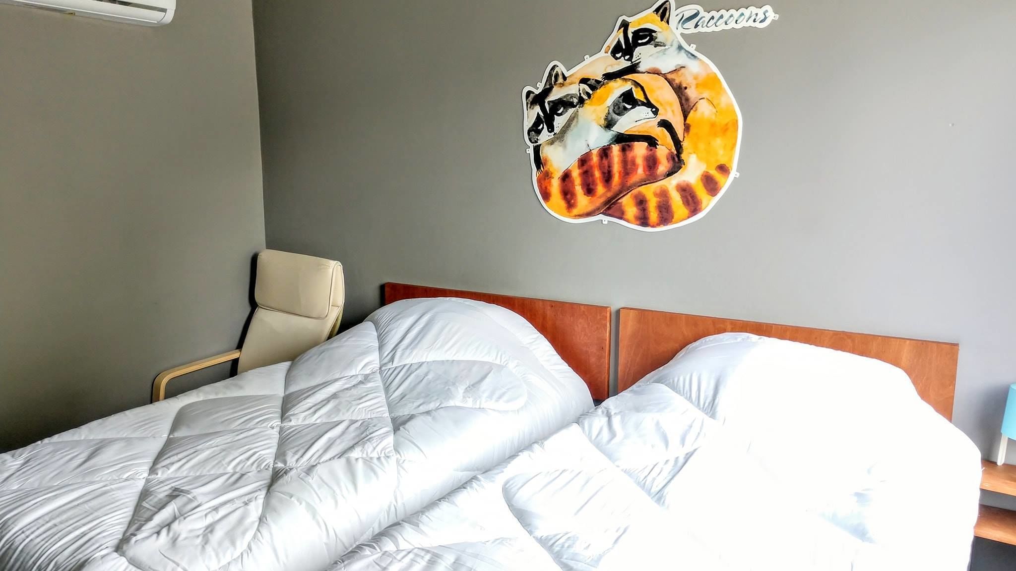 A hotel room with a bed, a chair, and a raccoon-themed wall decal.