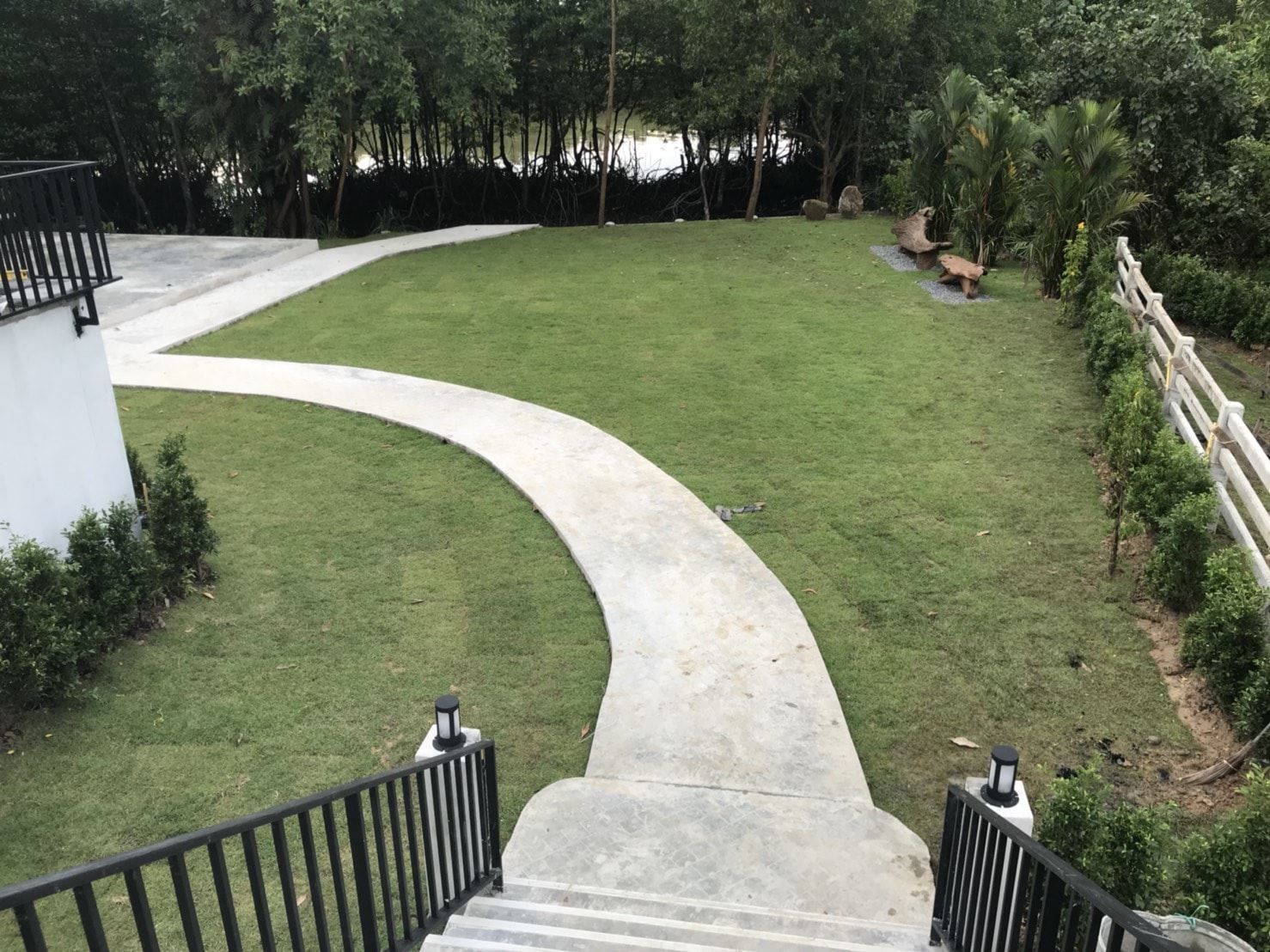 Un sendero de concreto curvo que lleva a una zona con césped, con un edificio blanco a la izquierda y una cerca blanca a la derecha.
