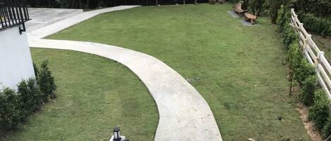 Een gebogen betonnen pad dat leidt naar een grasveld, met een wit gebouw links en een witte hek rechts.