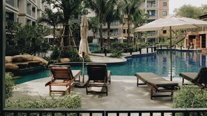A poolside area with lounge chairs, a small waterfall feature, and a view of a multi-story building in the background.