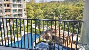 Uma varanda com vista para uma piscina, área de refeições e um edifício com várias varandas.