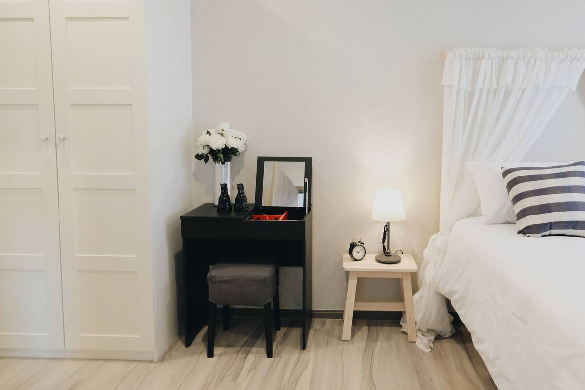 Ein Schlafzimmer mit Bett, Nachttisch, Lampe, Uhr und Schreibtisch mit Stuhl.