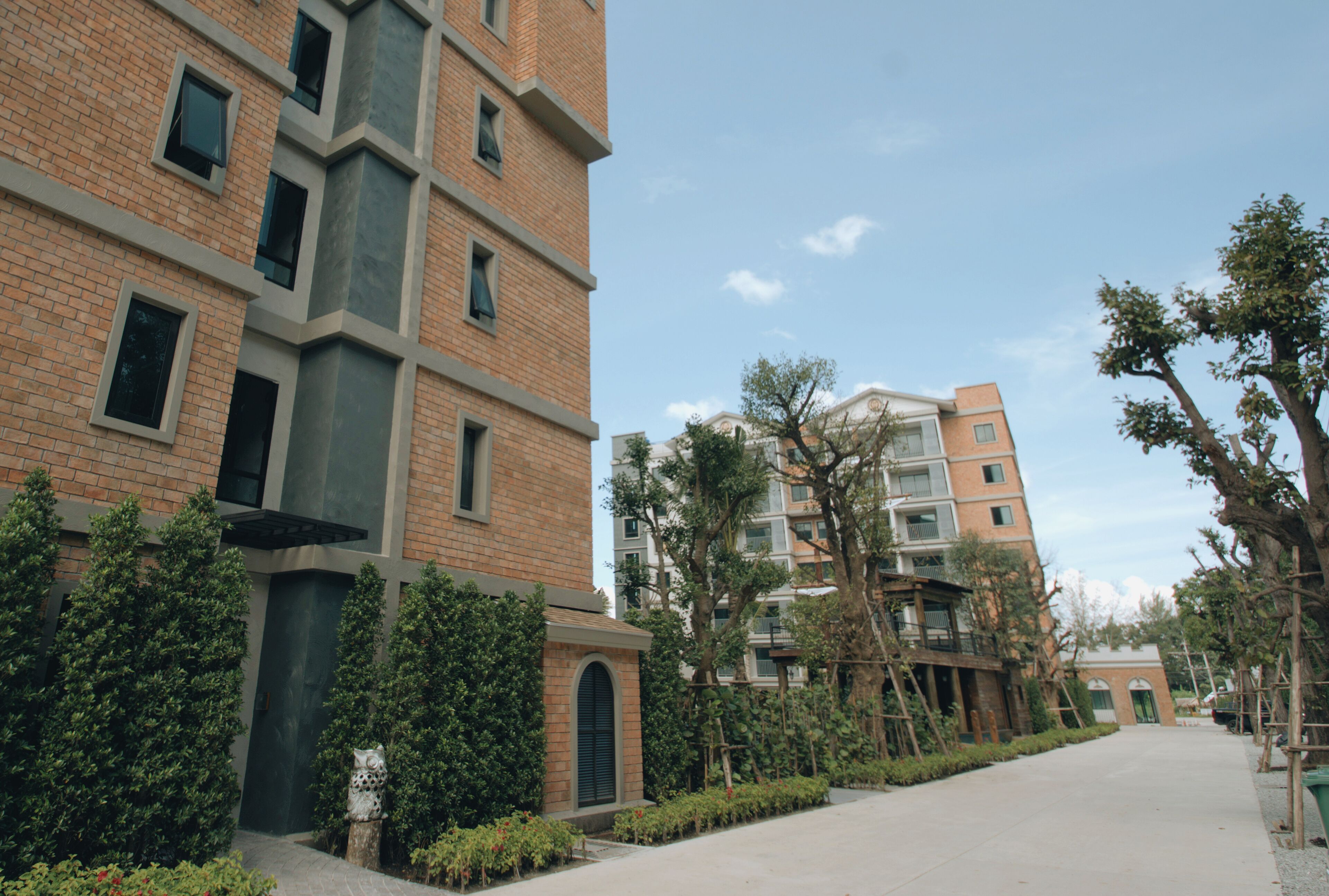 Um edifício moderno com fachada de tijolos, várias janelas e um caminho ladeado por árvores e arbustos.