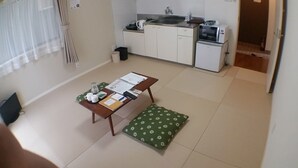 Una cocina pequeña y funcional con fregadero, microondas y refrigerador. En primer plano, una mesa de comedor con un cojín verde.