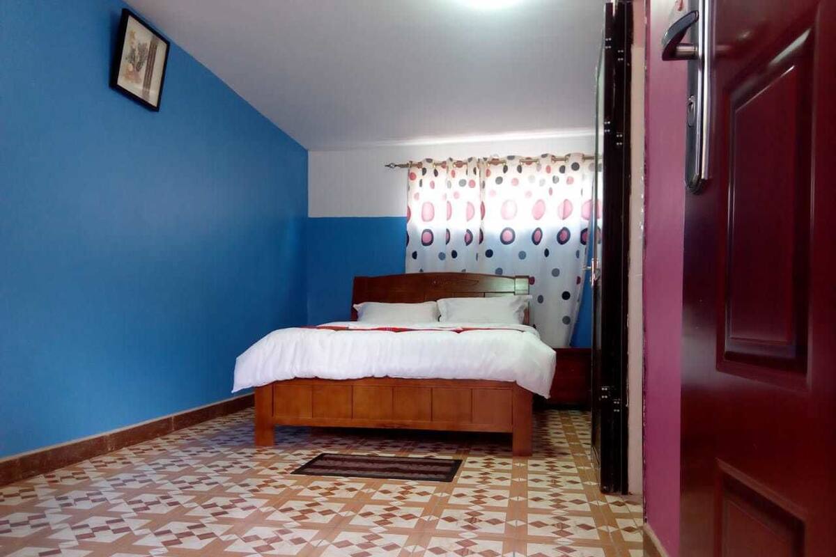 Un dormitorio con cama, cabecera de madera, suelo estampado y una puerta.