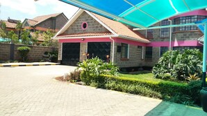 A building with a covered entrance, a gated driveway, and a well-maintained garden. - The Joshua Gardens (Nairobi)