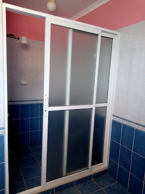 A bathroom with a frosted glass door, blue tiles, and a pink accent wall. - The Joshua Gardens (Nairobi)