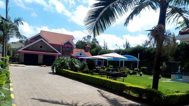 A paved pathway leading to a building with a red roof and a covered outdoor seating area. - The Joshua Gardens (Nairobi)