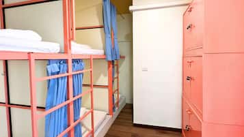 A dormitory room with bunk beds, a wardrobe, and a white refrigerator.