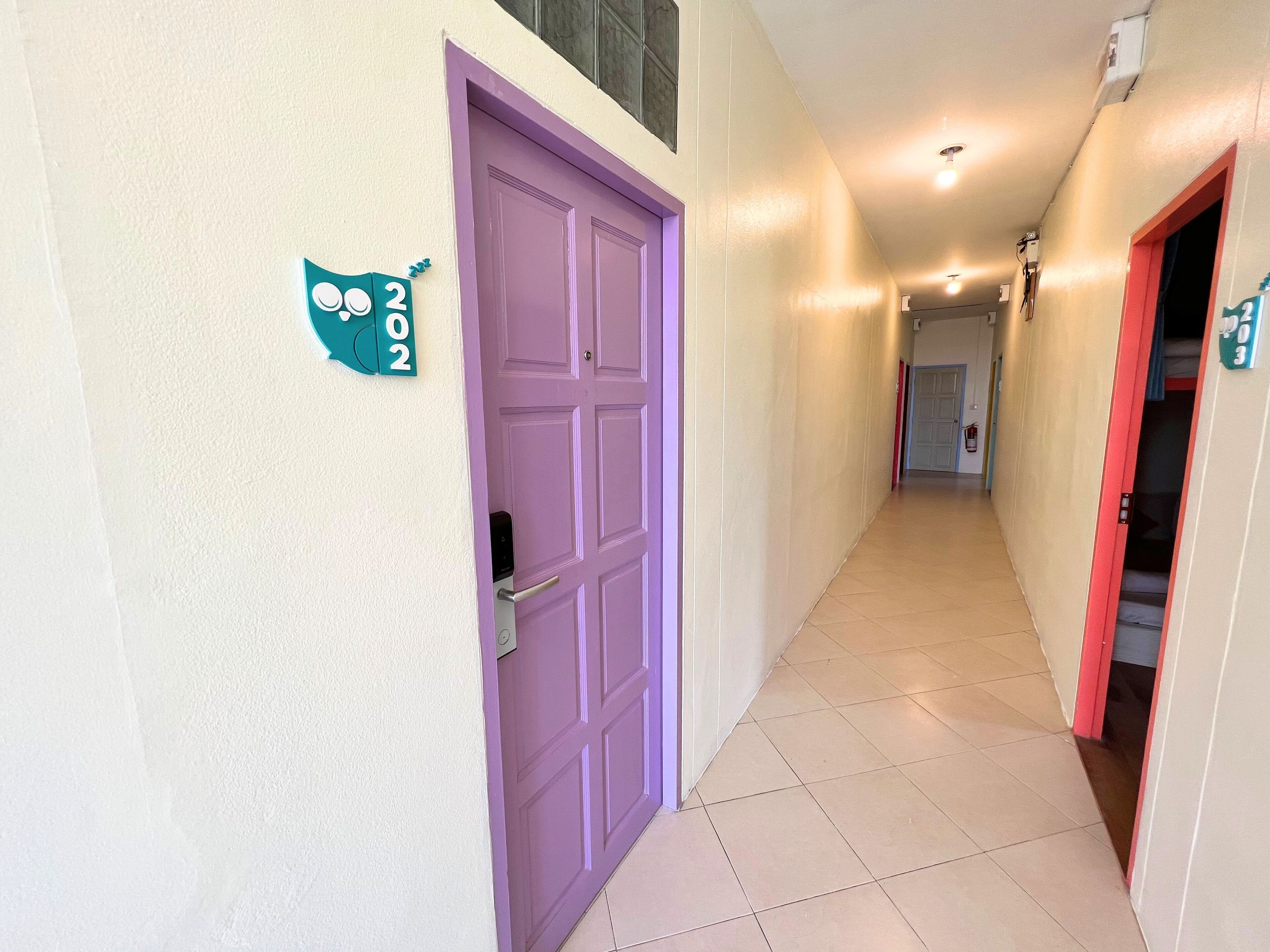 A hallway with a purple door, a sign indicating room number 202, and a staircase with a red frame.