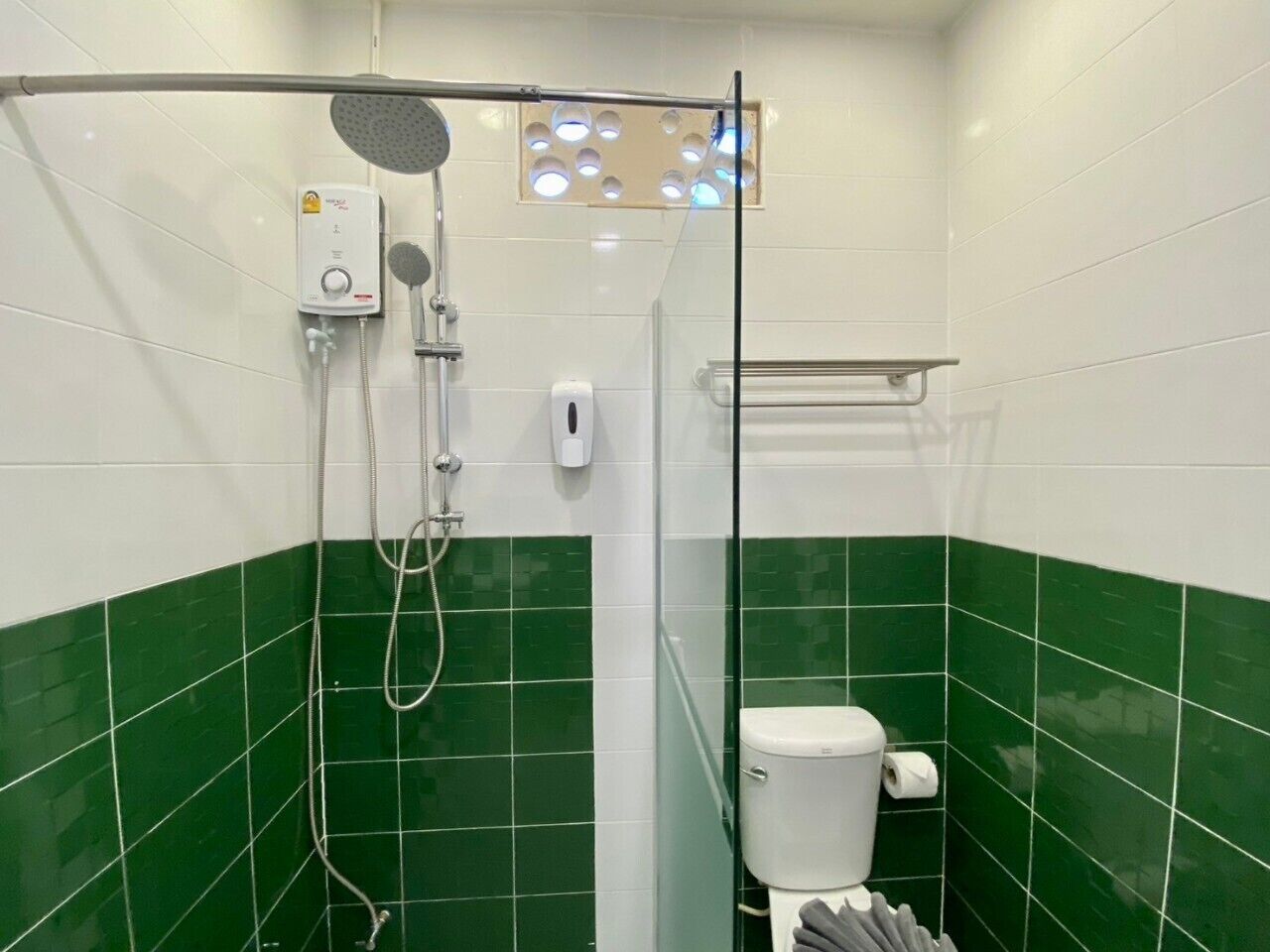 A bathroom with green and white tiles, a glass-enclosed shower, a toilet, and a hand dryer.