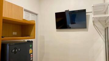 A compact kitchen with a refrigerator, a microwave, and a small wooden shelf.