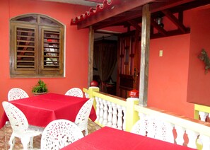 A room with a red table and white chairs, a wooden door, and a window with shutters. - Casa Salome (Viñales)