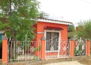 A house with a red exterior, a white metal gate, and a window with shutters. - Casa Salome (Viñales)