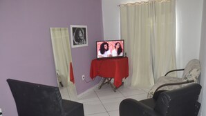 Una sala de estar con un televisor sobre una mesa roja, una silla negra y un sofá estampado.
