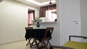 Comedor con mesa dispuesta para dos, un jarrón de flores y vistas a una cocina y una puerta.