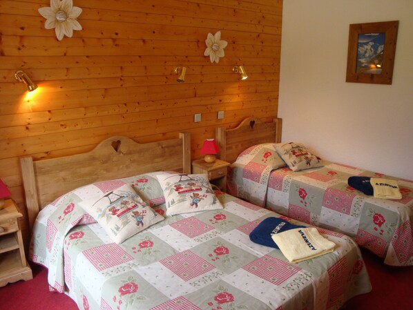 A cozy room with two wooden beds, each with floral bedding and pillows, a nightstand with a lamp, and a wooden wall with decorative flowers. - Azureva La Clusaz Les Confins (La Clusaz)