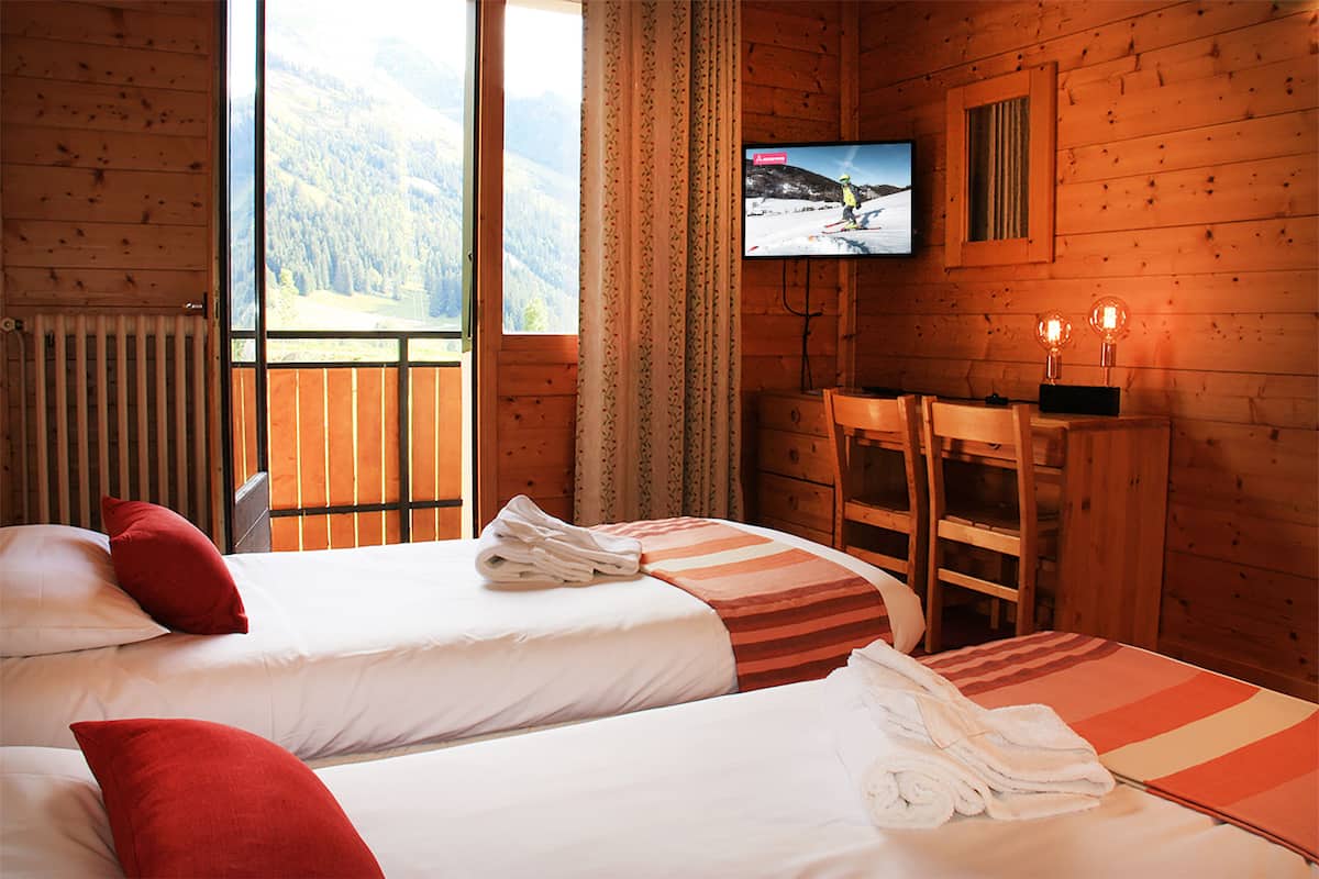 Habitación de cabaña de madera con dos camas, televisión y vista a una montaña nevada.