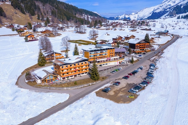 Un pueblo cubierto de nieve con un edificio anaranjado destacado, probablemente un hotel, que cuenta con varios pisos y balcones.