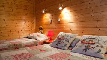 Une pièce chaleureuse aux murs en bois, avec deux lits dotés de draps à motifs floraux, une lampe rouge et des ours en peluche.