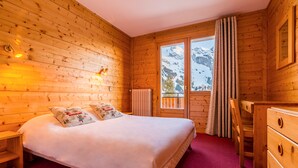 Una habitación de cabaña de madera con cama, cómoda y ventana con vistas a montañas nevadas.