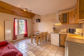 A compact kitchen with a dining area, wooden ceiling, and a small refrigerator. - Azureva Murol (Murol)