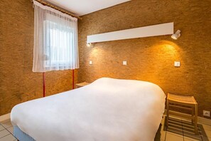 A bedroom with a large bed, a bedside table, a chair, a window with sheer curtains, and wall-mounted lighting. - Azureva Murol (Murol)